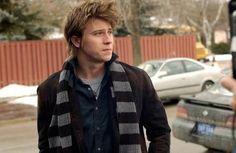 a young man standing in front of a parking lot next to a parked car and holding a camera