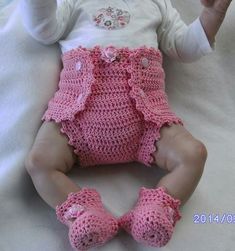 a baby doll wearing pink crocheted clothes on a white blanket with her hands in the air