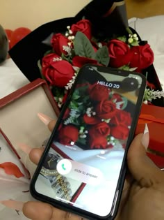 someone is holding their cell phone in front of some red roses and other gift boxes