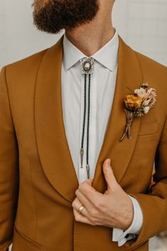 a man with a beard wearing a brown suit and flower boutonniere on his lapel