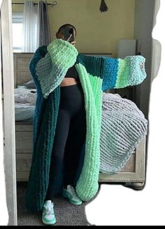 a woman standing in front of a bed wearing a green and blue knitted blanket