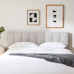 a white bed with two framed pictures on the wall above it and a plant next to it