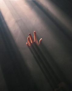 a person's hands reaching up into the air with sunlight streaming through them on a dark background