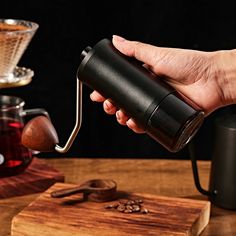 a person pouring coffee into a cup on top of a wooden table next to a grinder