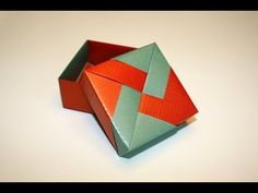 an origami box with red and green strips on the lid sitting on a white surface