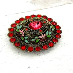 Authentic Vintage Little Nemo Oval Floral Brooch Pin Red Rhinestones Enamel SignedOutstanding colors and in excellent condition with minor enamel loss in tiny areas. All stones are present and original. Marked L/N on the reverse. A gorgeous rare brooch! This beautiful brooch measures 2 3/16 of an inch (55mm) by 1 15/16 of an inch (50mm). It is approximately 1/2 deep (13mm) deep at the center not including the pin stem.. Please see the photos for details and email us any questions.  Thank you for your interest! Red Enamel Brooch Pin, Red Enamel Brooch, Antique Red Brooch, Antique Red Brooch Jewelry, Vintage Red Pins For Gifts, Vintage Red Pins As Gift, Vintage Red Pins For Gift, Traditional Red Brooch For Gift, Traditional Red Brooches For Gifts