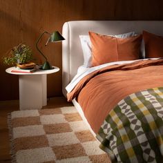 a bed with an orange comforter and pillows on top of it next to a white table