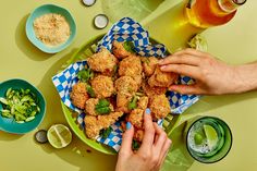 two hands reaching for fried food on a plate next to beer and bowls with other foods