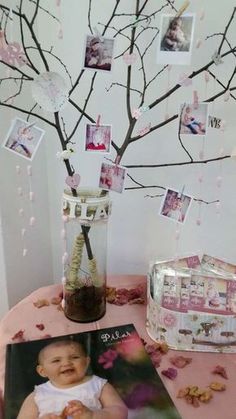 a baby is sitting in front of a tree with pictures hanging from it's branches