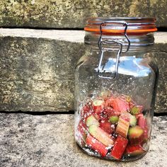 a glass jar filled with sliced fruit sitting on top of a cement slab next to a stone wall