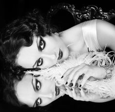 black and white photograph of two women laying on a chair with feathers around their necks