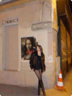 a woman standing in front of a building with a poster on the wall behind her