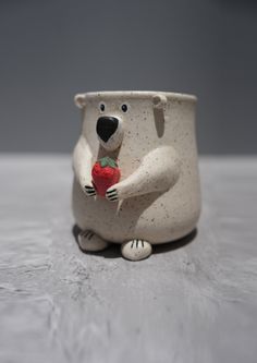 a ceramic polar bear holding a strawberry in its paws and sitting on top of a table