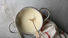 a whisk in a pot with a wooden spoon next to it on a towel