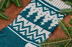 a blue and white knitted scarf sitting on top of a wooden table next to pine branches