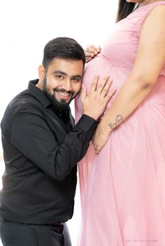 a pregnant woman in a pink dress poses with her husband