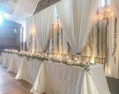 the table is set up with white linens and greenery on it, along with candles