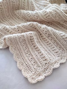 a white crocheted blanket laying on top of a bed next to a pillow