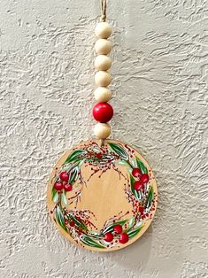 a wooden ornament hanging on a wall decorated with holly berries and white beads