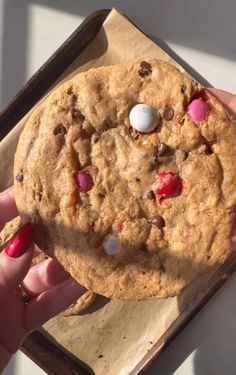 a person holding a chocolate chip cookie with candy on it's side and one hand