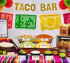 a taco bar is set up with mexican food and decorations on the wall behind it