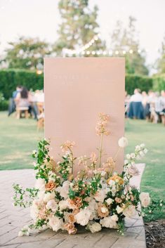 a sign with flowers and greenery on it in the middle of a lawn area