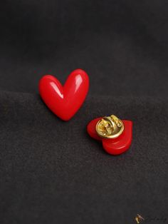 two red heart shaped buttons sitting next to each other on a black surface with a gold button