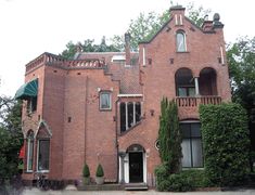 an old red brick building with ivy growing on the front and side windows, surrounded by greenery