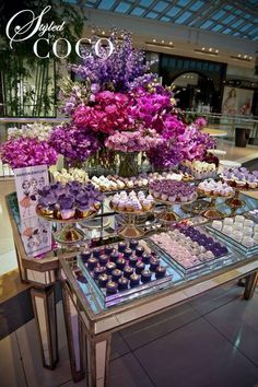 a table filled with cupcakes and purple flowers