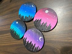 four painted rocks sitting on top of a wooden table with trees and the moon in the sky