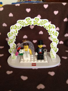 two legos are sitting in front of a wedding arch with hearts on the background