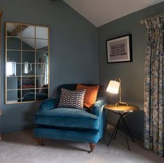 a living room with a blue chair, mirror and lamp on the wall in front of it