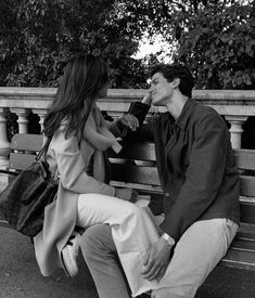 a man and woman sitting on a park bench talking to each other while holding hands