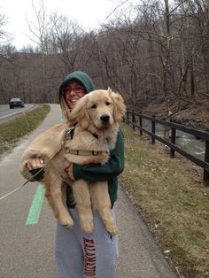 a person holding a dog in their arms on the side of a road next to a forest