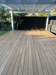 an empty wooden deck in the middle of a yard with a pergolated roof