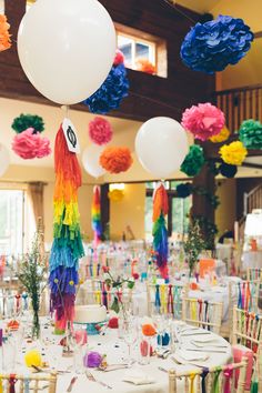 a room filled with lots of tables covered in white table cloths and colorful paper flowers