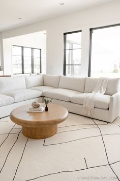 a living room with white couches and large windows in the back ground, along with a rug on the floor