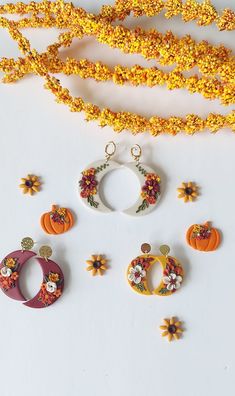 an assortment of earrings and necklaces on a white surface next to yellow flowers, leaves and beads