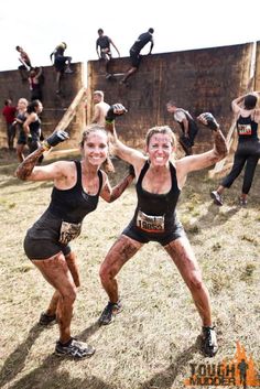 two women with mud on their faces and arms are posing for the camera in front of an obstacle course