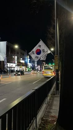 a city street at night with cars driving on the road and flags in the air