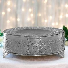 an ornately decorated silver cake dish on a white tablecloth with lights in the background