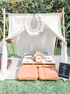 an outdoor table set up for a party with white draping and orange cushions