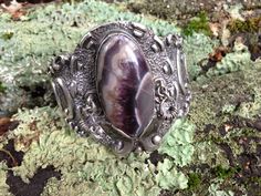 a silver ring with a purple stone in the center on mossy rocks and leaves