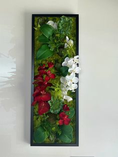 an arrangement of flowers is displayed in a black frame on the wall next to a remote control