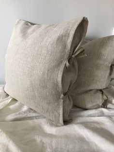 two pillows on top of a bed with white sheets and linens in the background