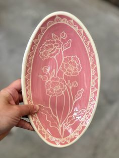 a hand is holding a pink and white plate with flowers on the inside, in front of a gray background