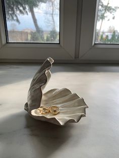 two gold wedding rings sitting in a shell on a table next to a window sill