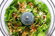 a food processor filled with lots of green vegetables and ingredients to make a healthy salad