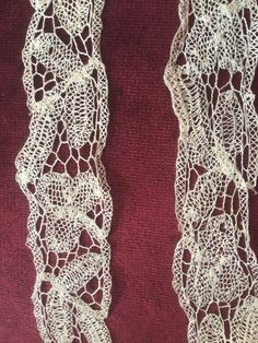 two pieces of white lace sitting on top of a red cloth covered in crochet