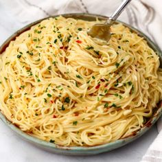 a bowl filled with pasta and topped with parsley sprinkles on a white cloth